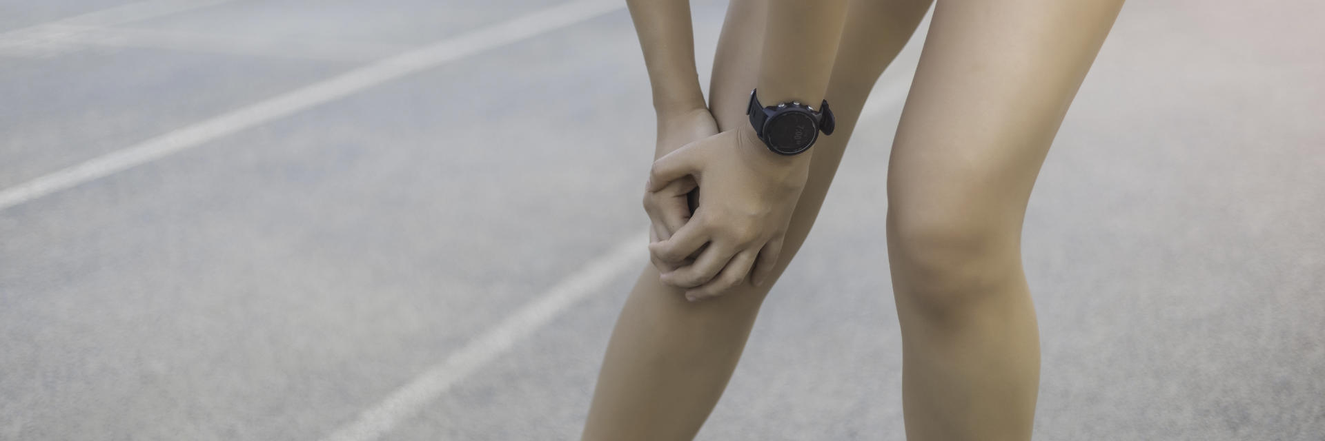 An sportsperson standing on the running track and touching the painful knee area.