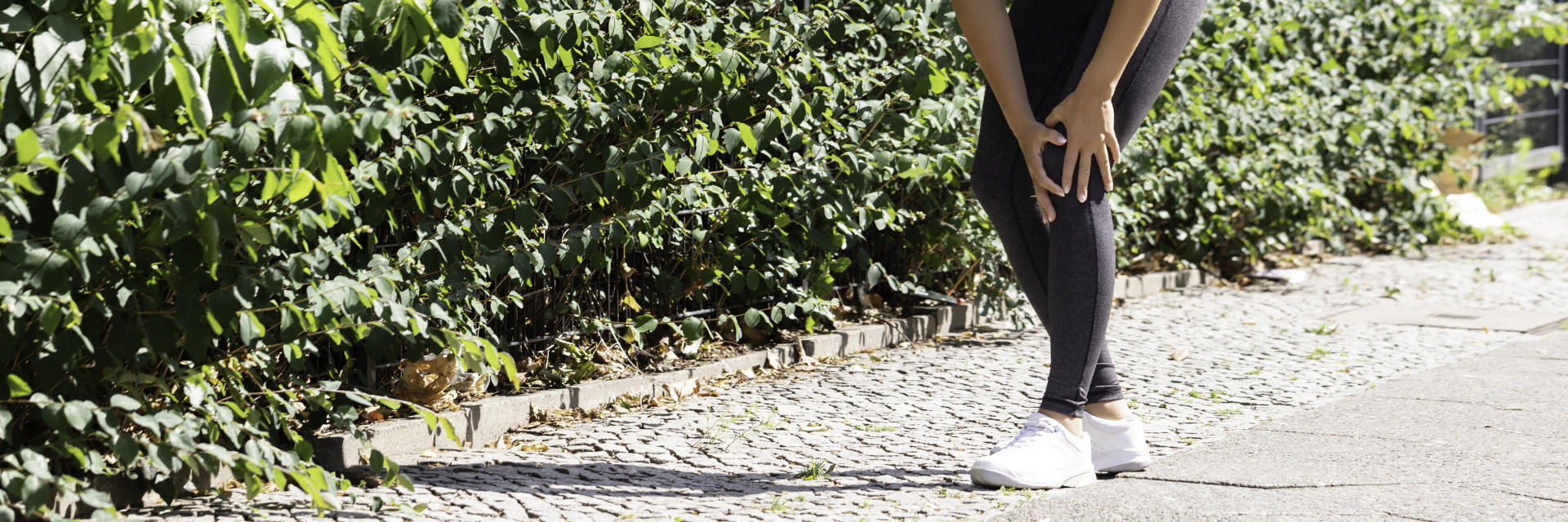 A jogging woman with knee pain touching the painful knee.