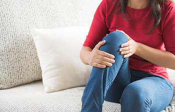 woman sitting on sofa and feeling knee pain